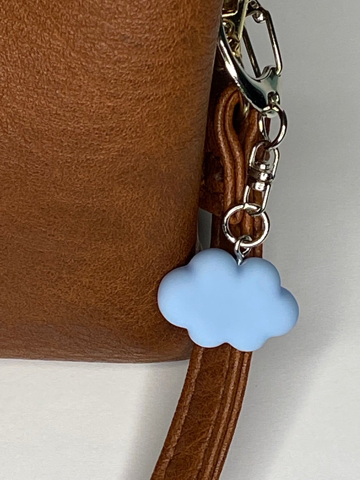 Brown leather bag with a blue cloud charm on a light gray background