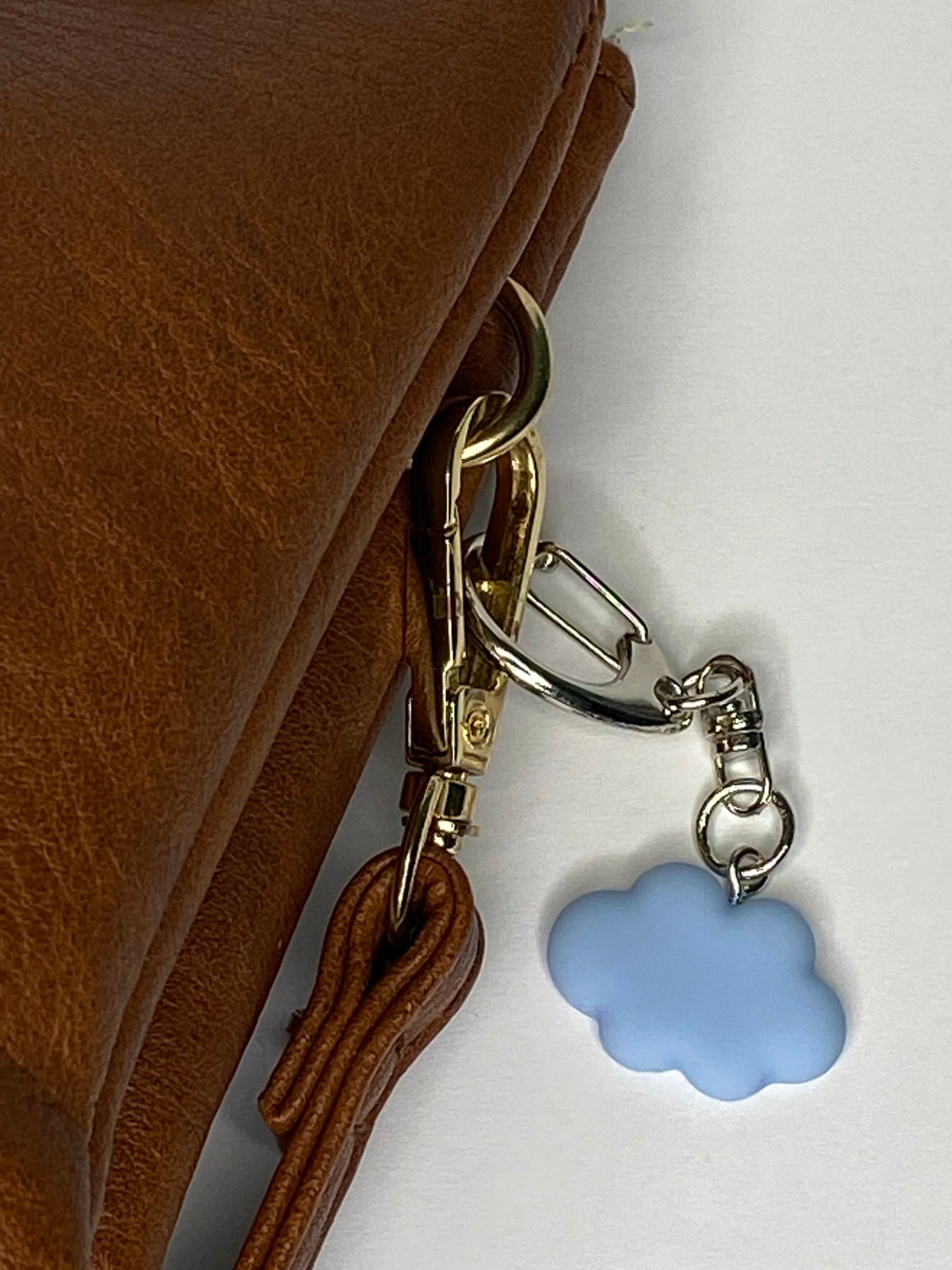 Brown leather handbag with a gold clasp and blue flower charm on a white background
