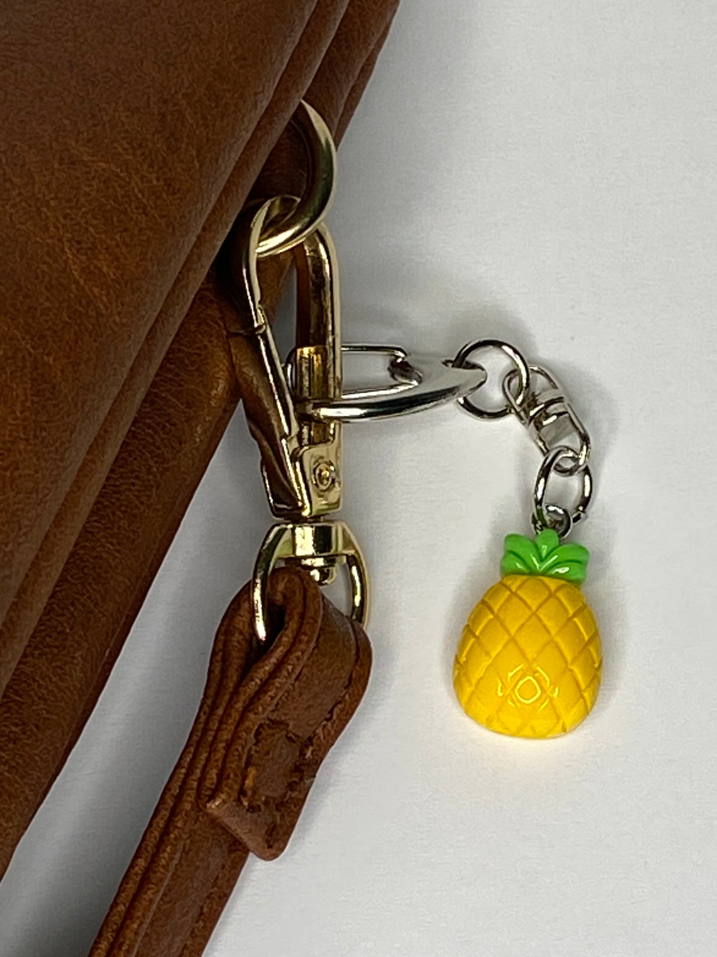 Pineapple-shaped keychain attached to a brown leather bag.