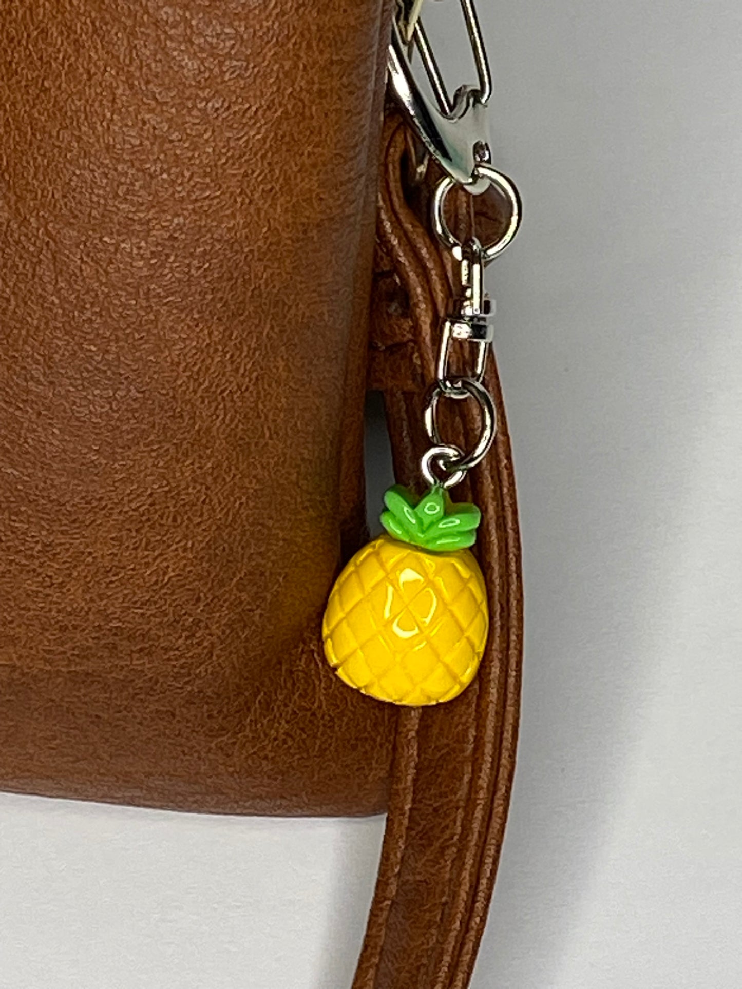 Brown leather bag with a pineapple-shaped keychain on a neutral background