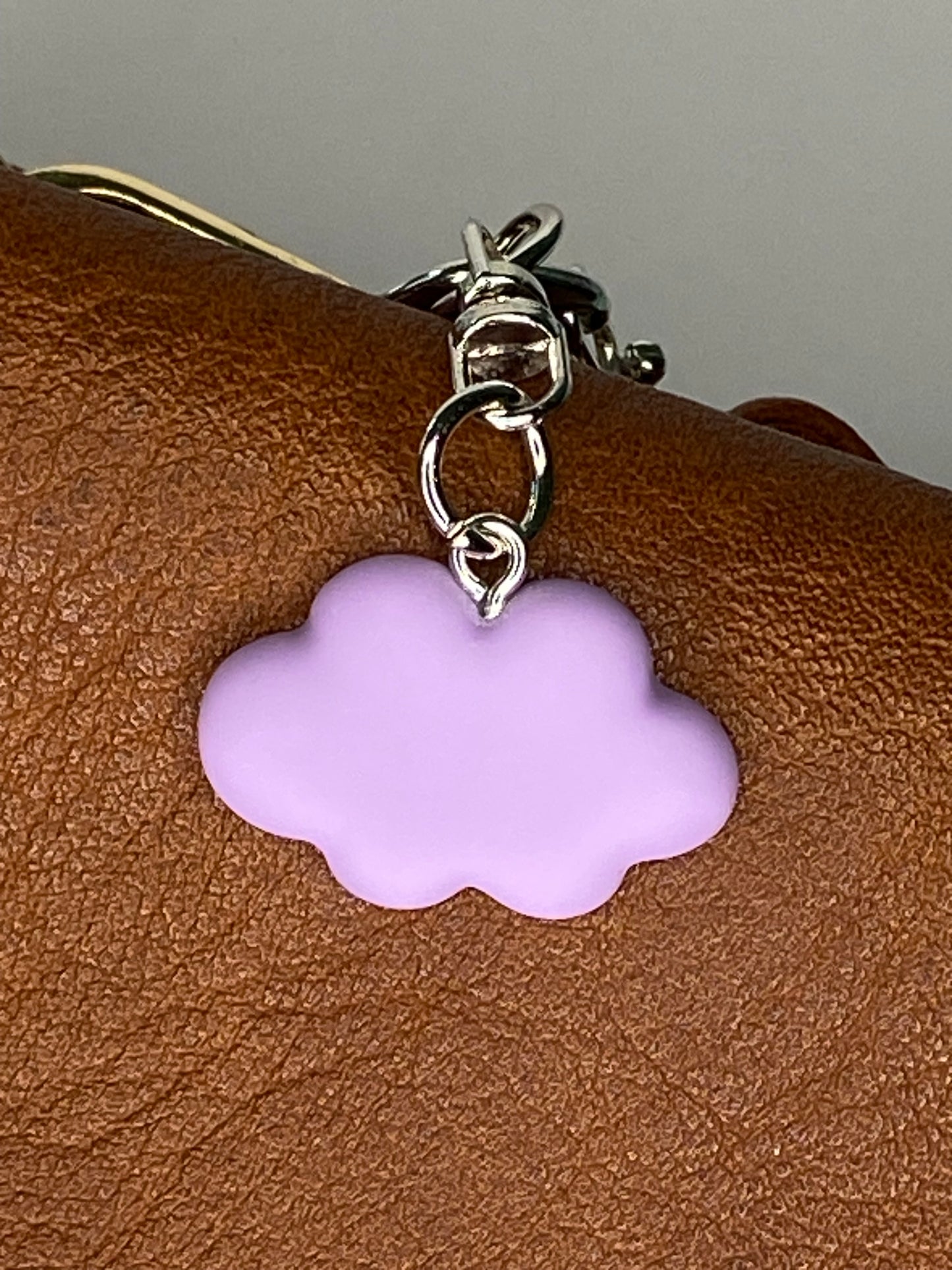 Purple cloud-shaped charm on a silver chain against a brown leather background