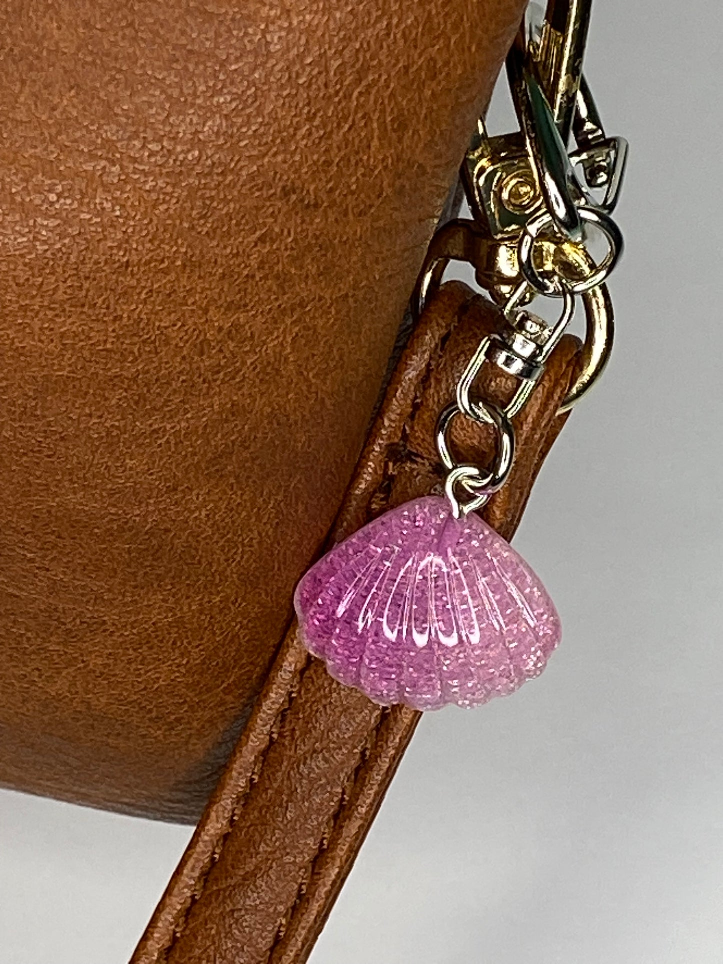 Brown leather bag with a violet seashell charm on a gray background
