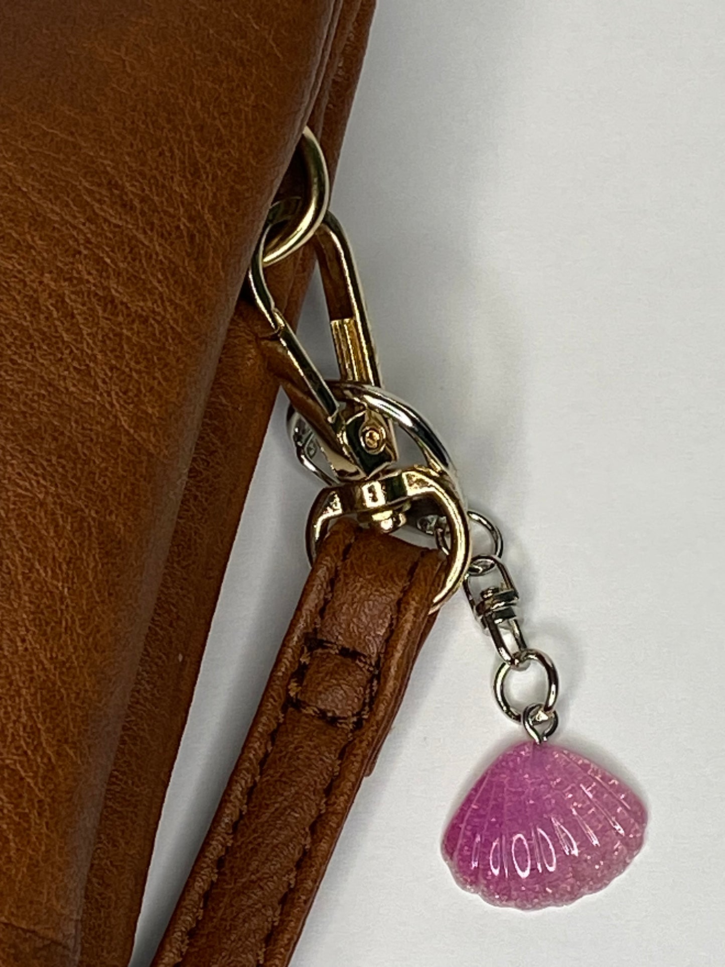 Close-up of a brown leather bag with gold hardware and a violet seashell charm on a white background