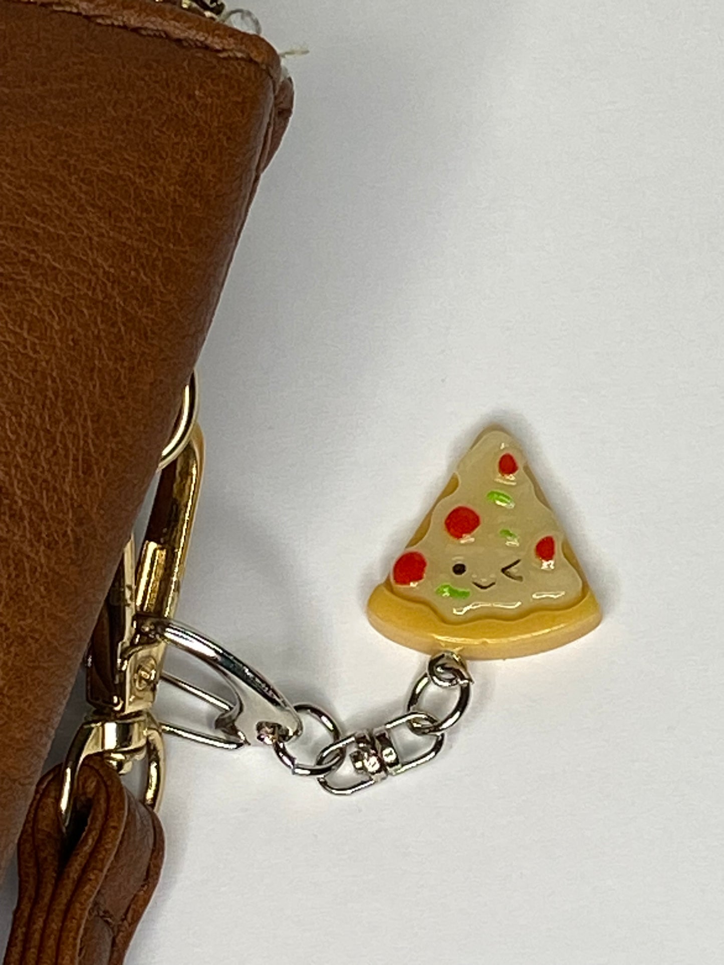 Pizza slice keychain attached to a brown leather bag on a white background