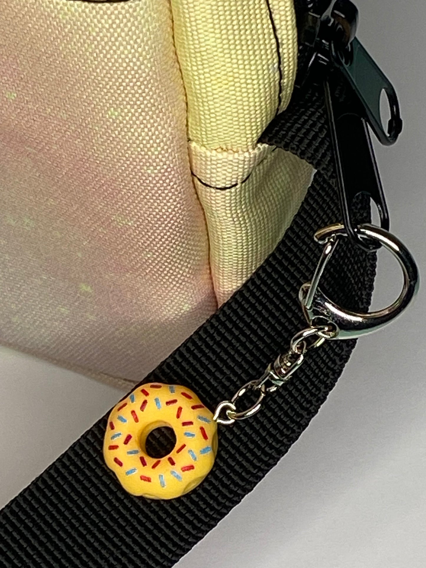 Yellow donut charm on a black strap attached to a pastel bag.