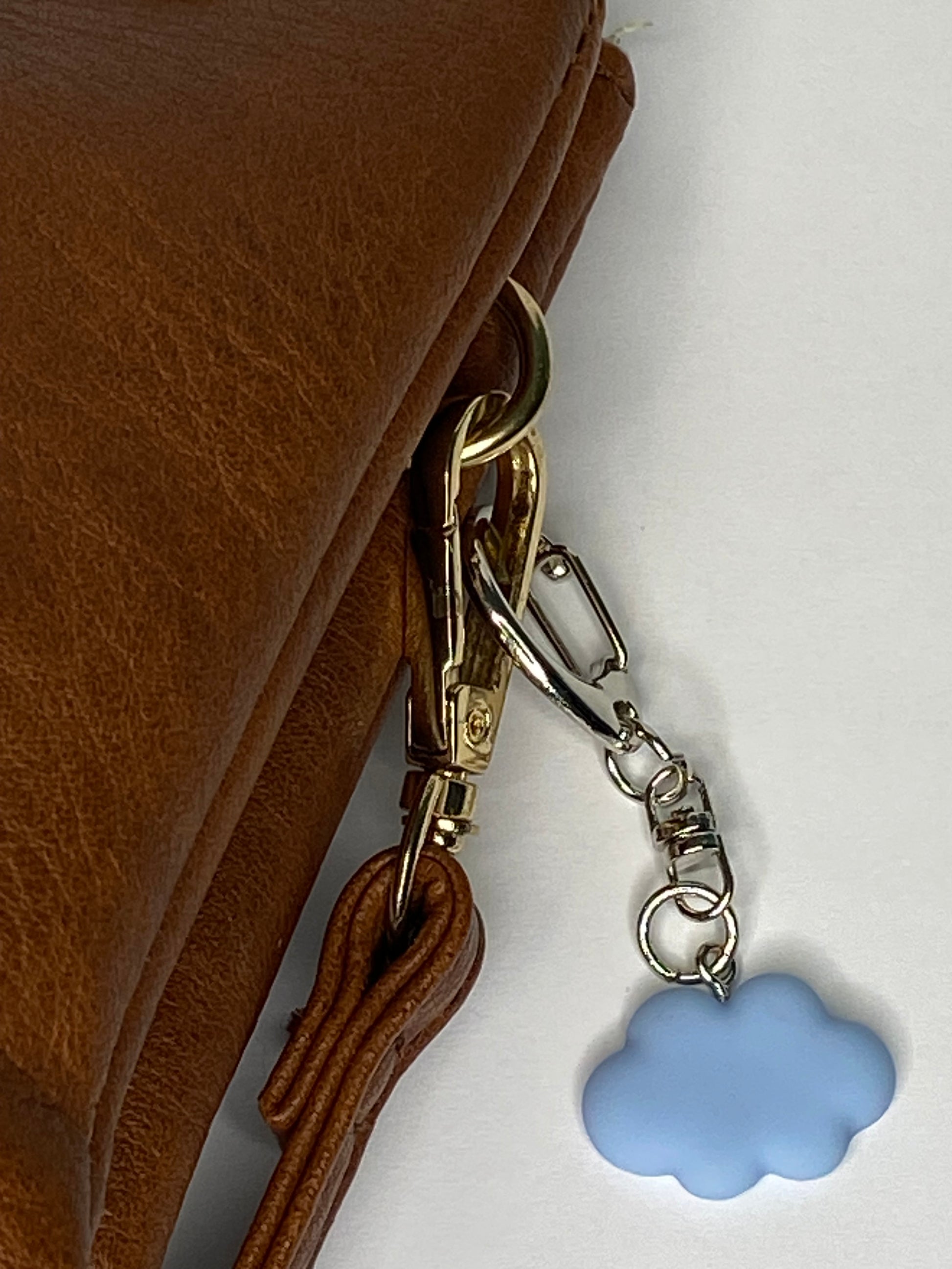 Brown leather handbag with a gold clasp and blue cloud-shaped charm on a white background