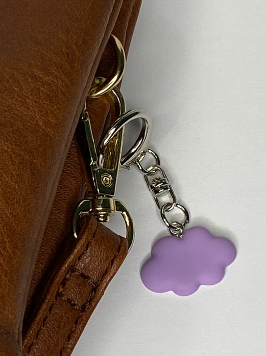 Brown leather bag with gold clasp and purple cloud-shaped keychain on a white background