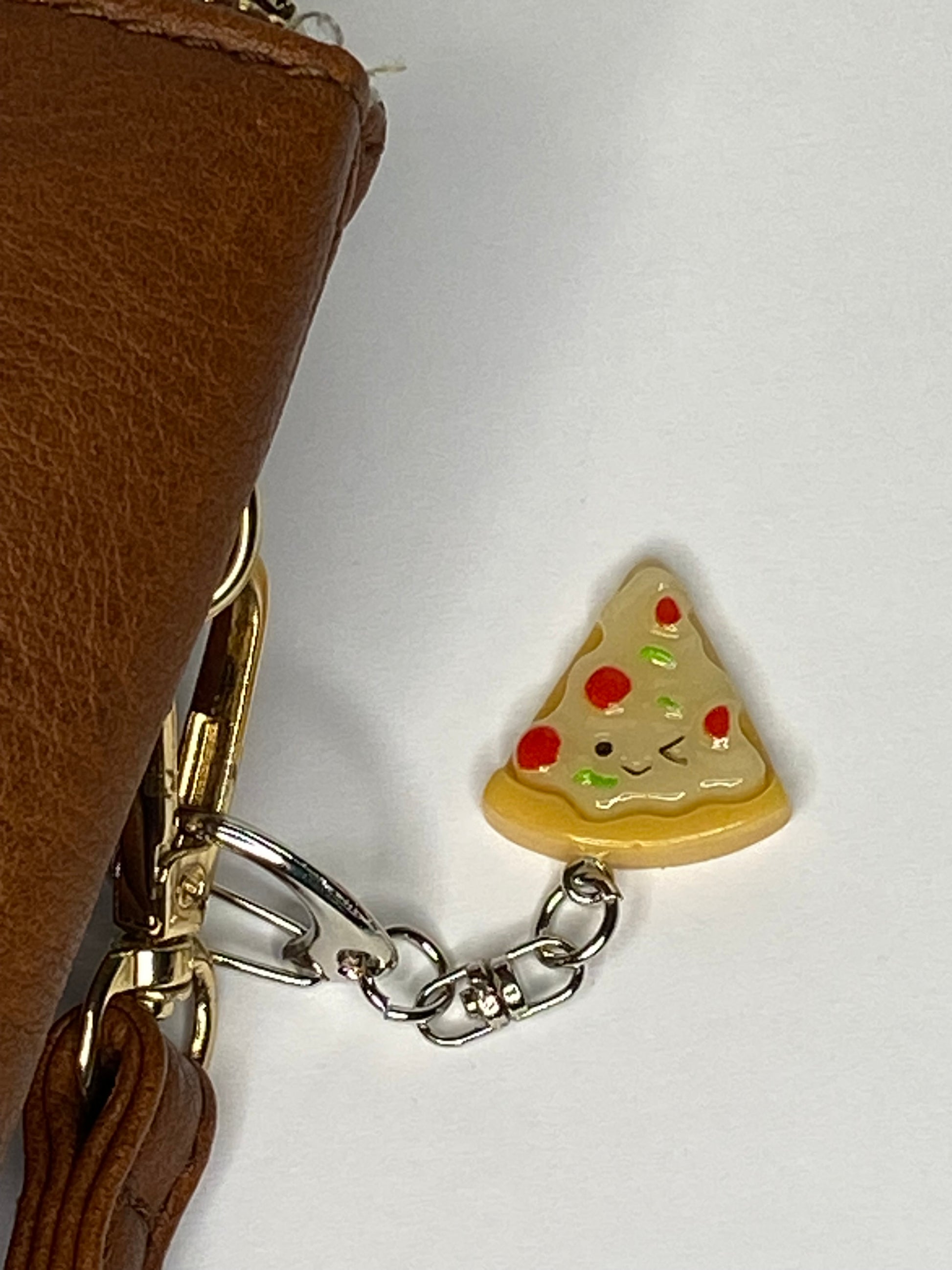 Pizza slice keychain attached to a brown leather bag on a white background